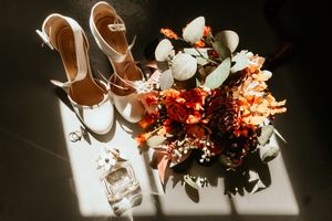 Wedding bouquet and white heels arranged in dramatic lighting with shadows cast on a light surface.