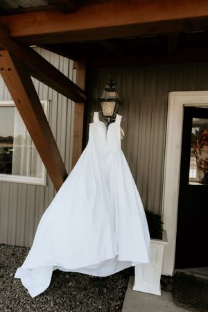 Multiple white wedding dresses hanging on display outside a rustic wooden building.