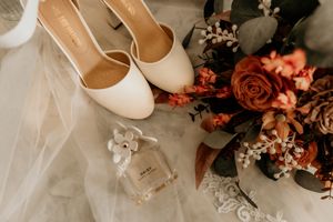 A collection of elegant white wedding shoes displayed with autumn-colored floral arrangements and delicate lace details.
