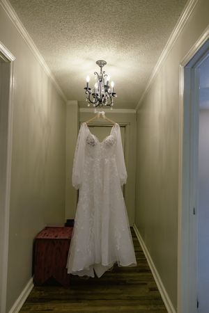 Elegant lace wedding dress with long sleeves hanging from a chandelier in a softly lit hallway.