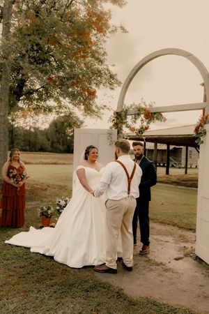 Wedding party poses under outdoor archway during autumn wedding celebration.