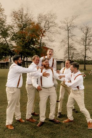 Groomsmen in white shirts and khaki pants perform a playful domino-falling pose sequence on grass.