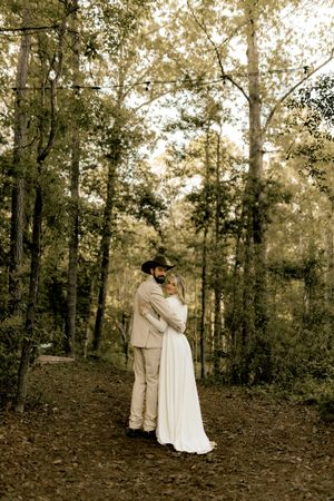 Newlywed couple embraces on a wooded forest path surrounded by tall trees at golden hour.