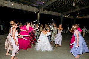 Bride in white wedding dress dancing with guests in colorful dresses at outdoor reception party at night. Elli brell farms, Pikeville, NC.