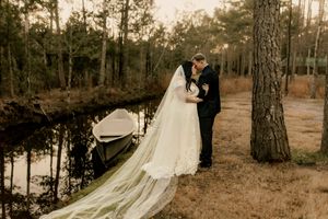 A romantic wedding couple embraces in a serene forest setting with warm sepia tones and tall pine trees.
