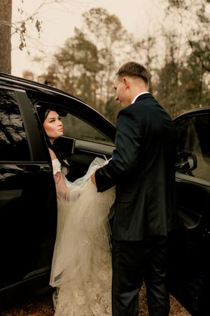 A couple shares an intimate moment by their car at dusk, with the bride wearing a white dress and groom in dark suit.