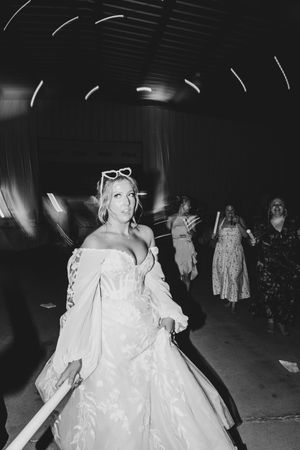 Black and white photo of a bride in a ball gown with sunglasses on her head dancing at a wedding reception.