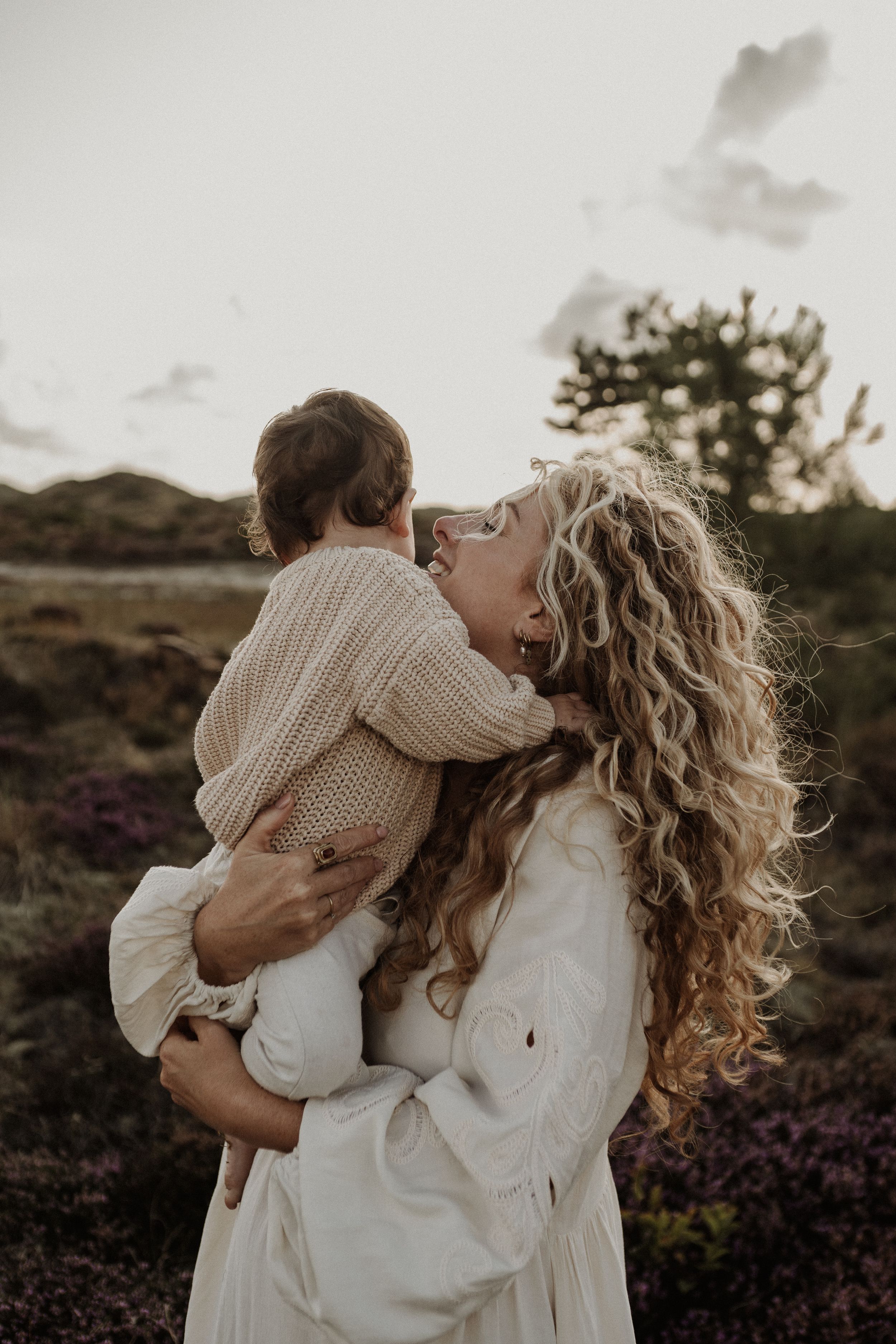 A tender moment captured at sunset with a parent and child embracing in a field of purple heather.