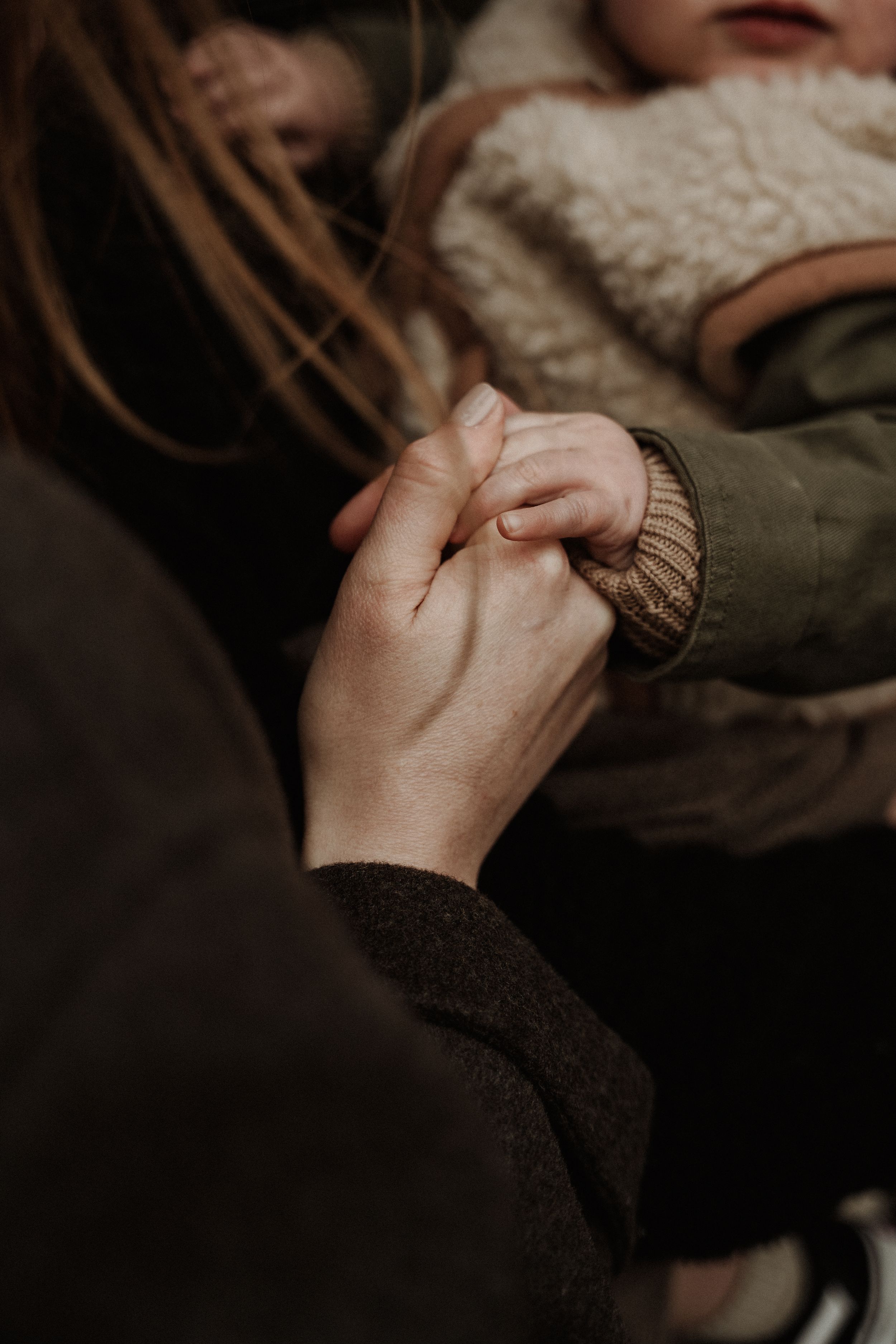 Close-up shot of hands holding each other tenderly, wearing warm knit sweaters in moody lighting.
