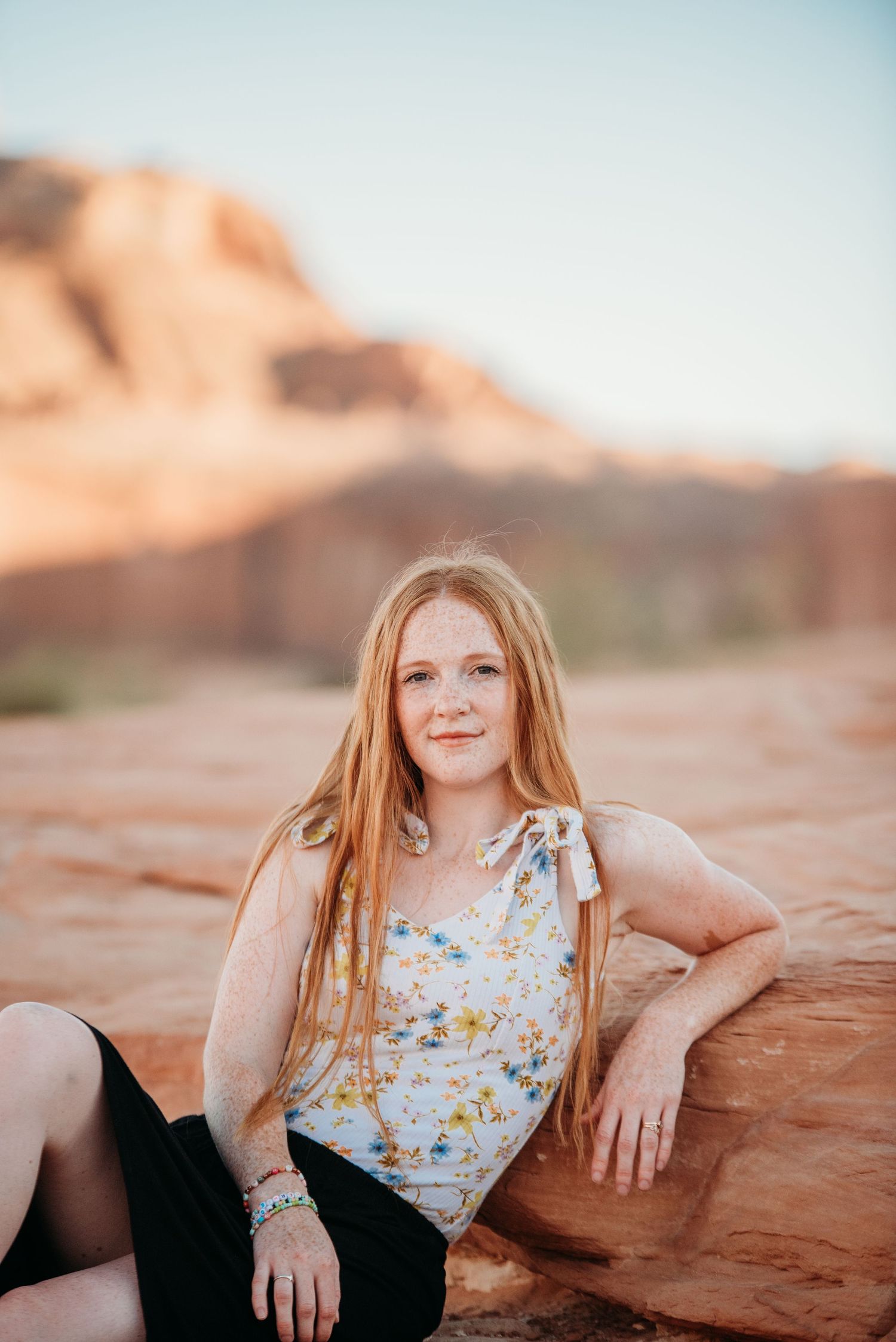 Portrait of someone in a floral top sitting on red rock formations during golden hour.