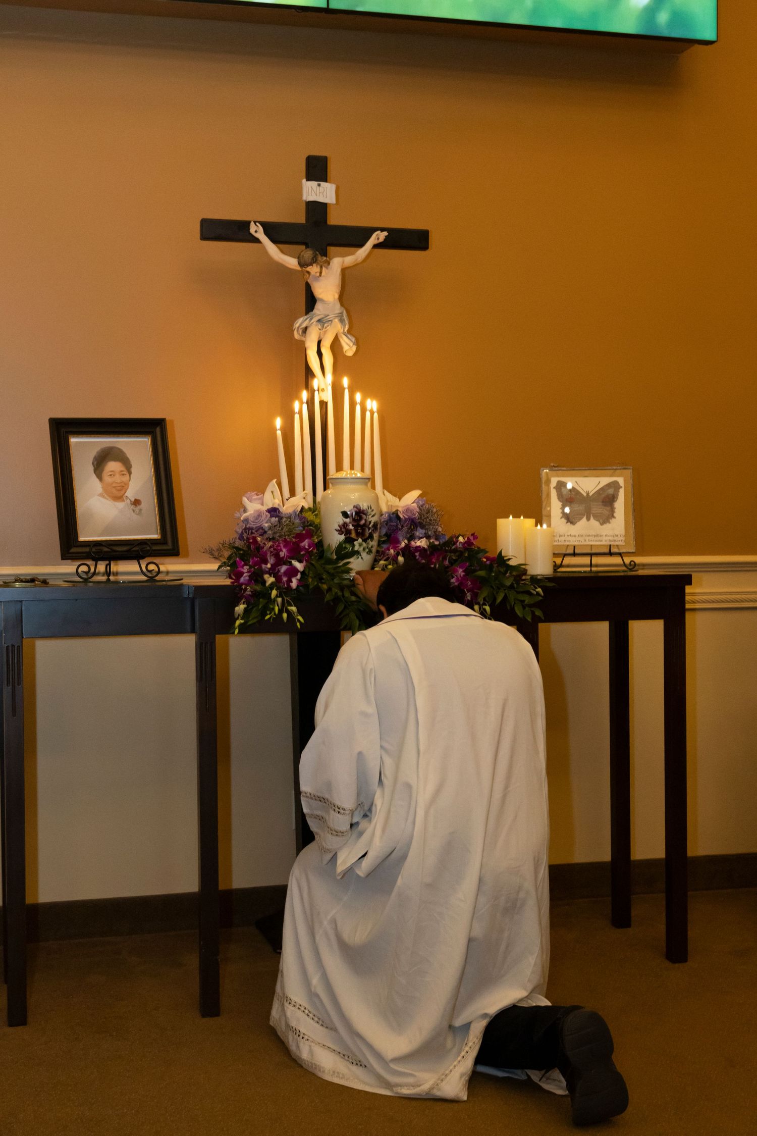 Priest kneeling to a urn with candles surrounding it