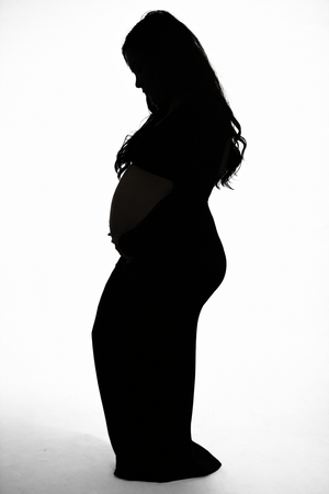 Elegant black and white silhouette of pregnant woman standing and cradling baby bump.