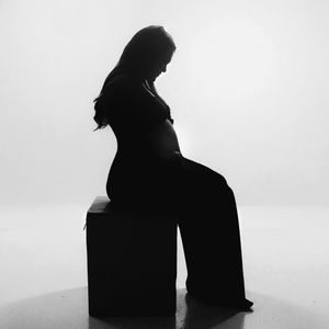 Black and white silhouette of pregnant woman sitting on a cube against white background.