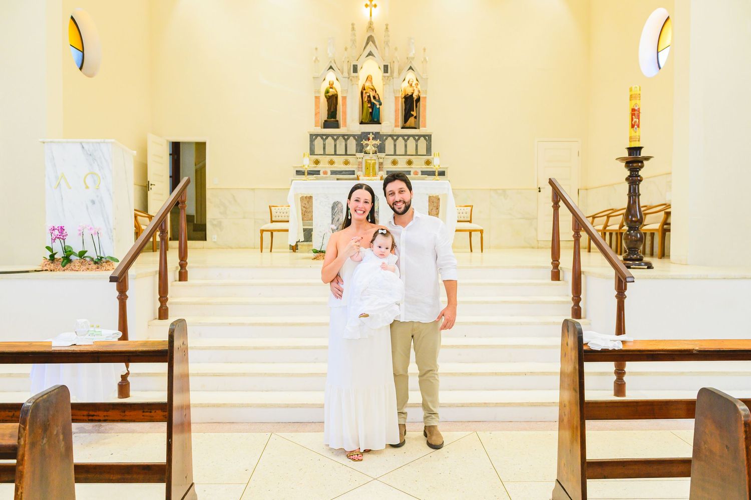 A couple stands together on white marble steps inside a church with a golden altar and wooden pews.