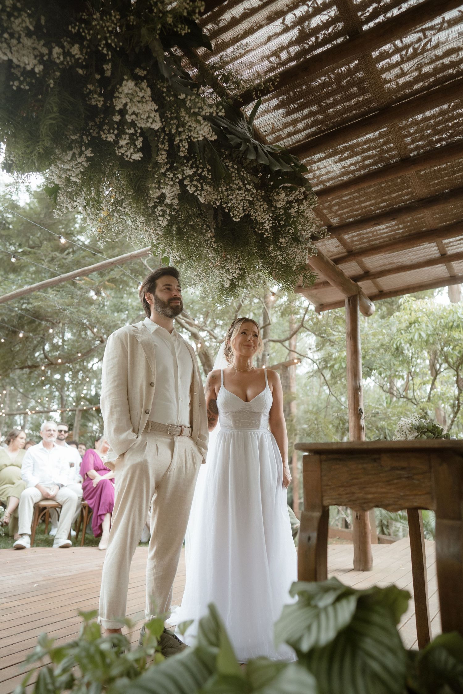 A wedding ceremony under a rustic wooden pergola decorated with lush greenery and flowers.
