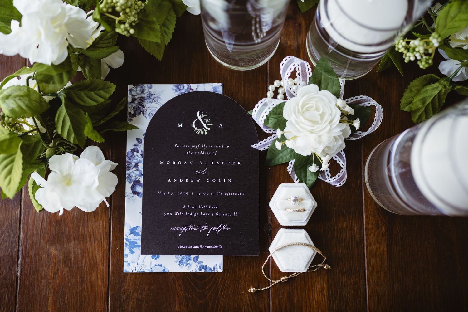 Wedding invitation on dark wood table with white floral decor and hexagonal glass vessels.