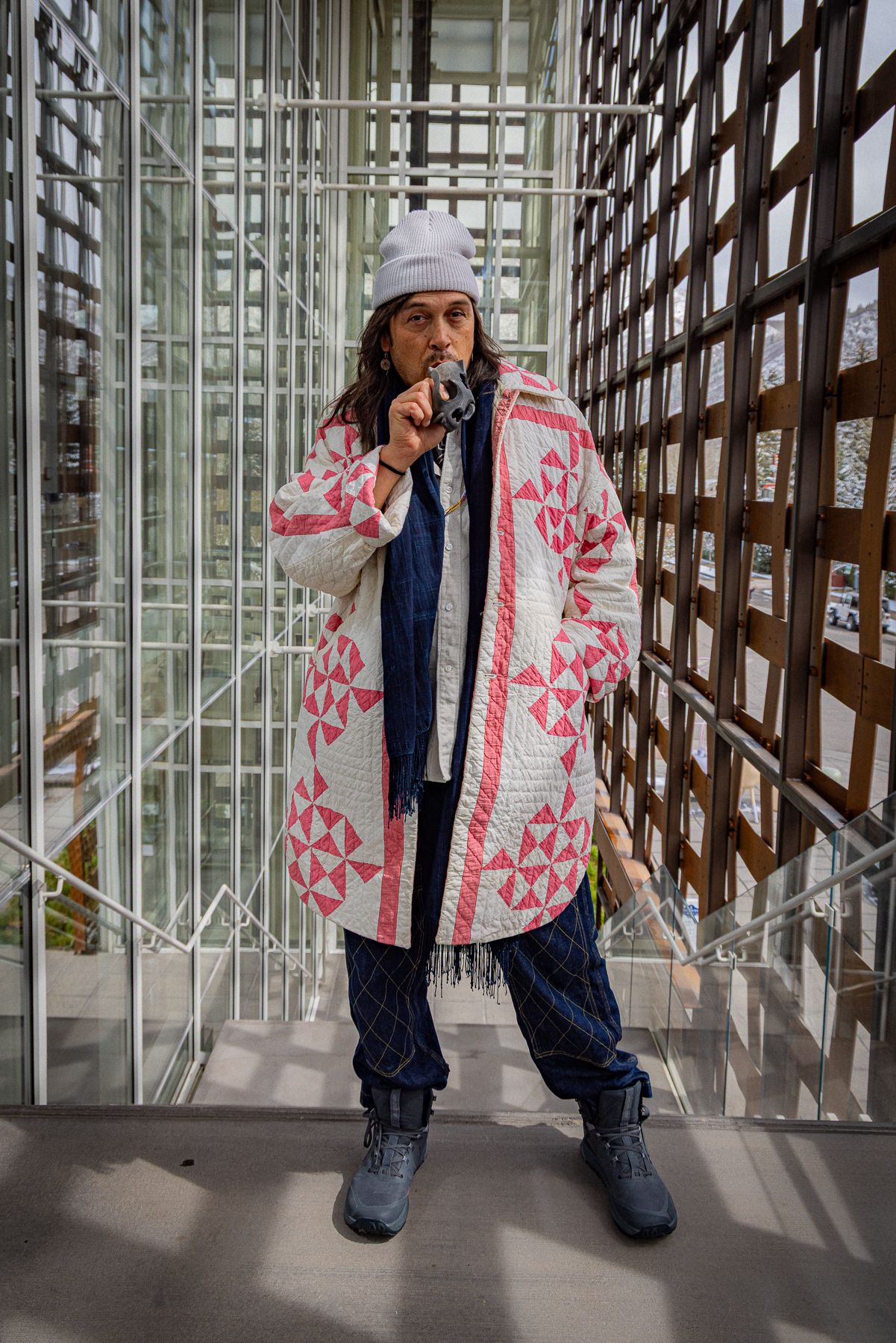 Someone in a pink patterned winter coat and jeans stands in snowy scenery with aspen trees and buildings in the background.