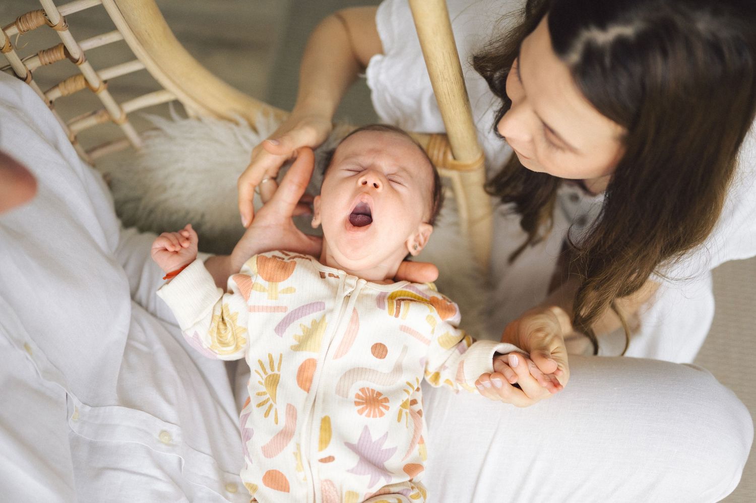 Baby in pajamas yawning and stretching while lying on white bedding.