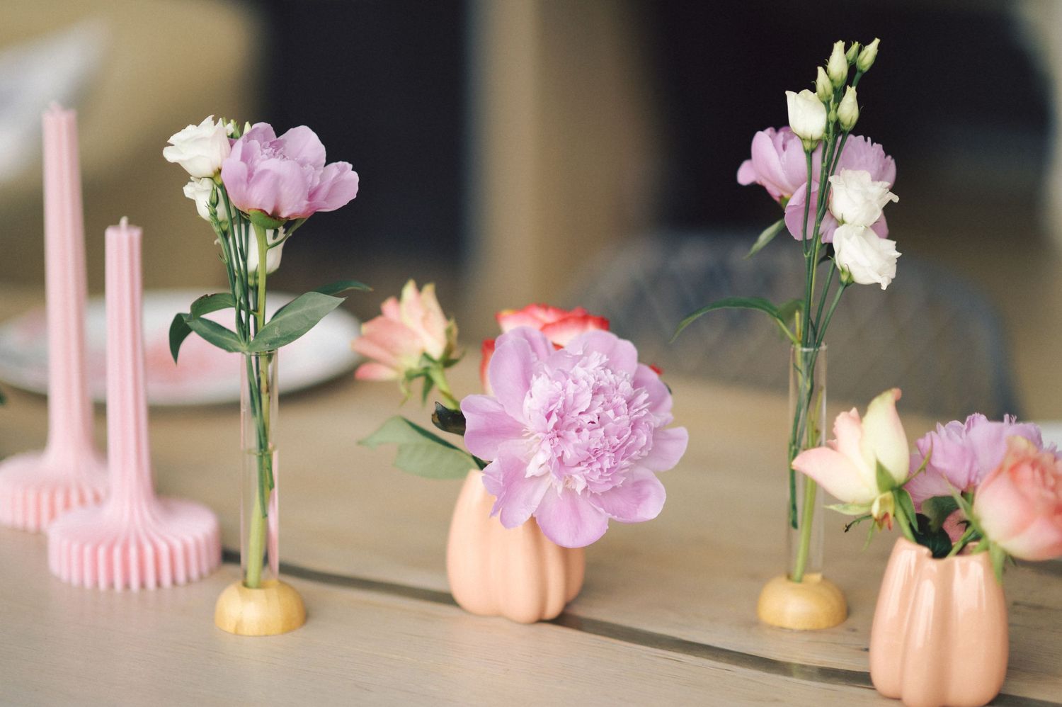 Pink carnations and delicate flowers arranged in small peach-colored vases with pink candles on display.