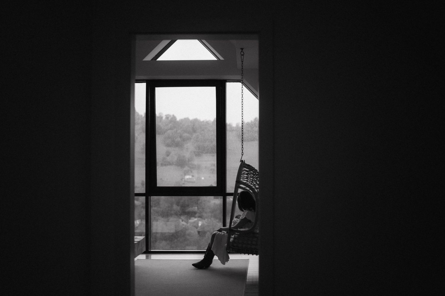 A silhouetted chair sits in front of a bright window in a dark room, creating a moody black and white contrast.