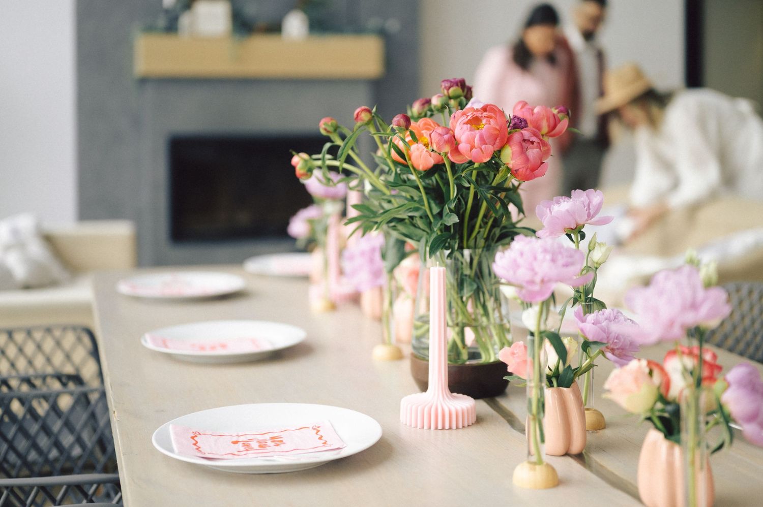 An elegant table setting with pink flowers in vases and decorative plates arranged on a wooden dining table.