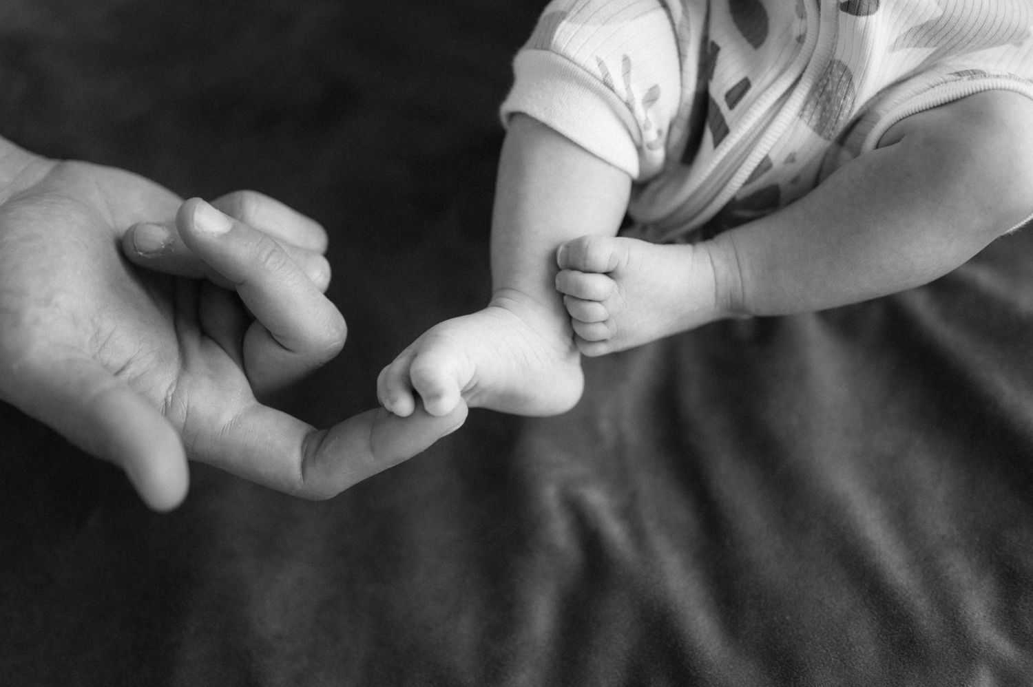A tender black and white photo showing a tiny baby foot being gently touched by an adult finger.