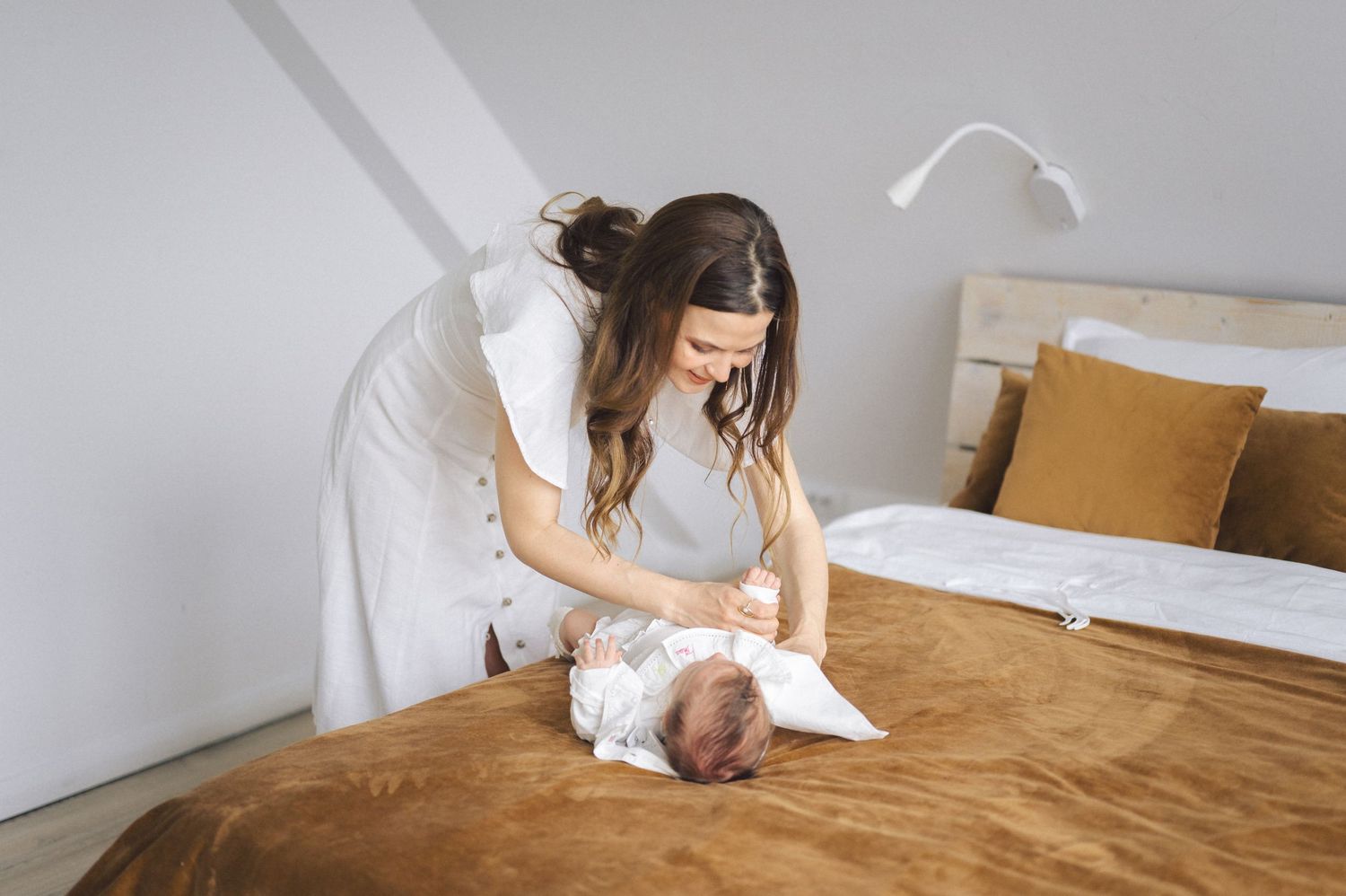 A healthcare worker examines and cares for a patient on a brown bed in a minimalist room with white walls.