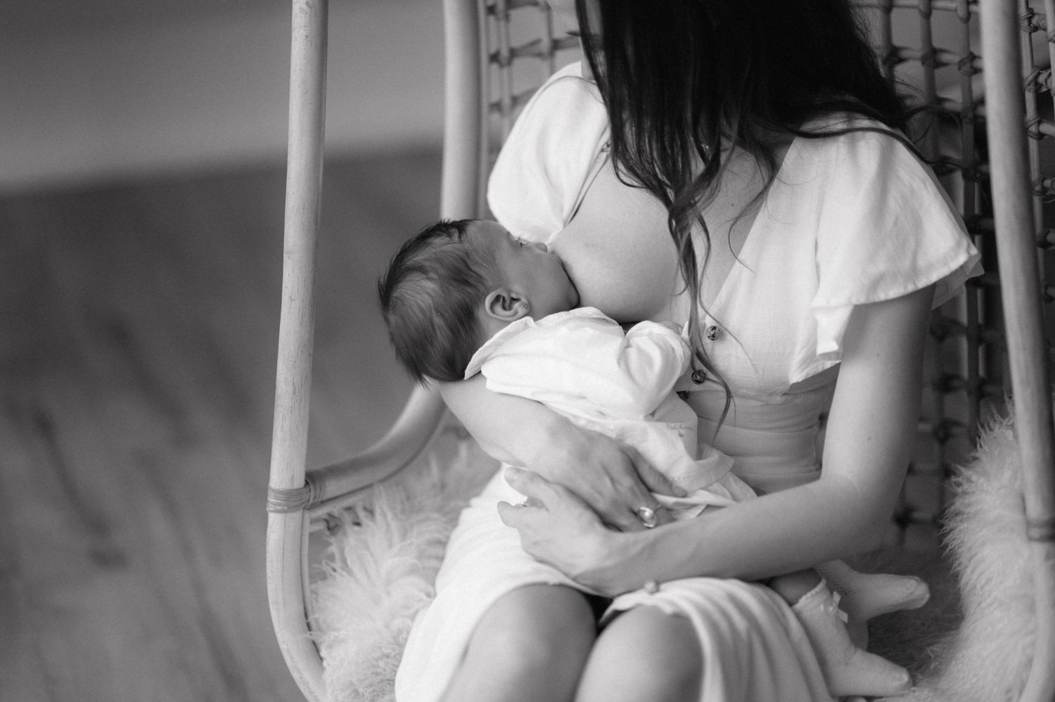 Black and white photo of a mother nursing her baby while sitting in a rocking chair during an intimate moment.