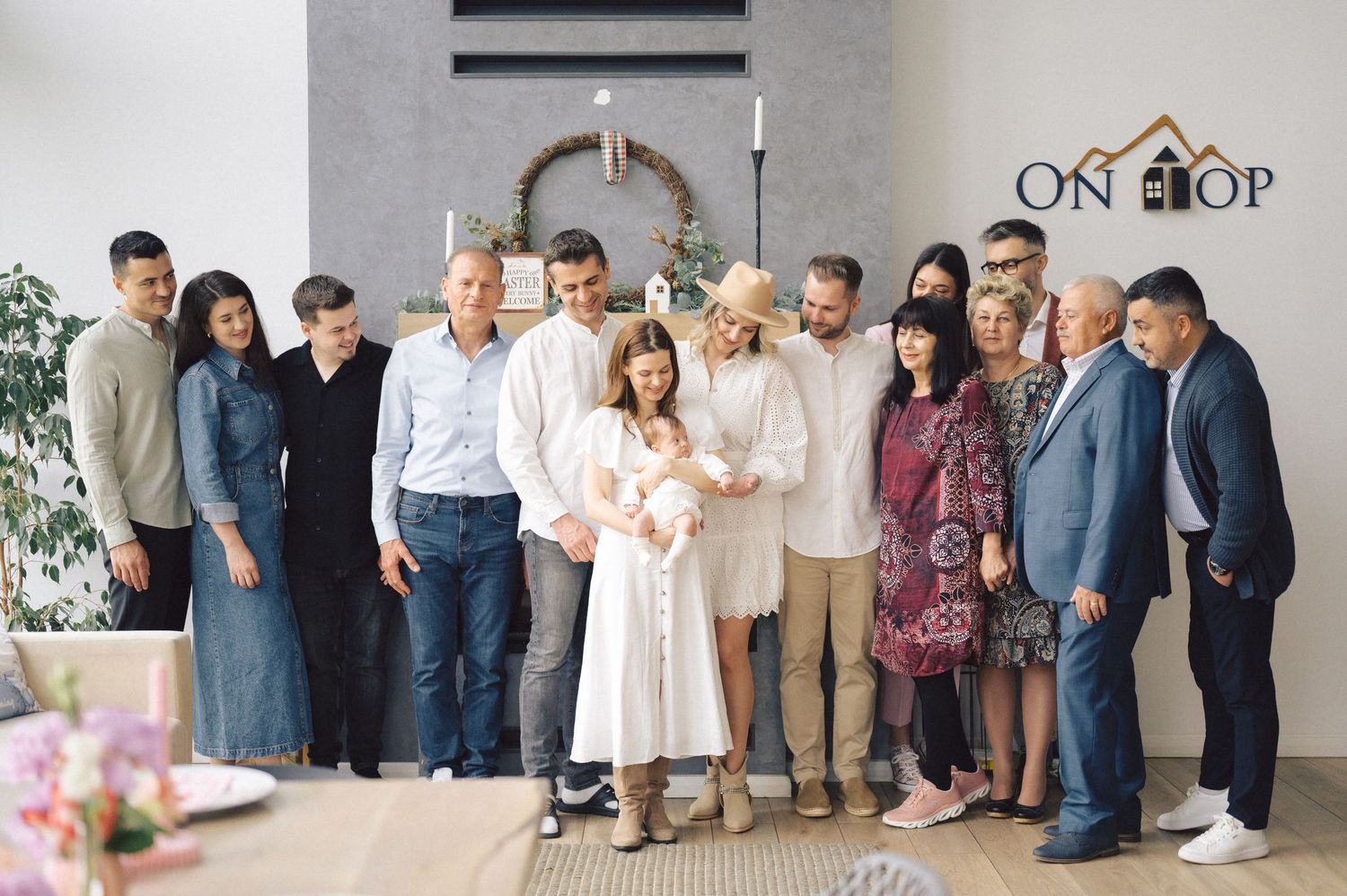 A group of people gathered together wearing casual and formal attire in a bright interior space with floral decor.