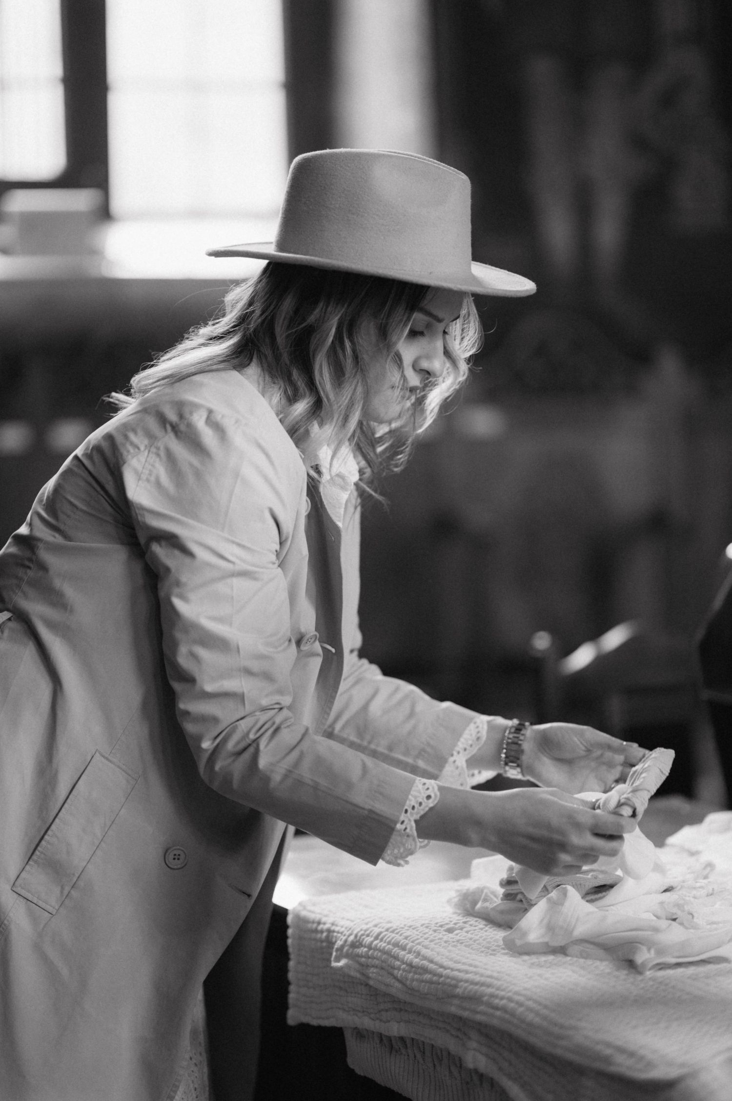 A person in business attire and a fedora hat leans over a table while reading documents in black and white photograph.