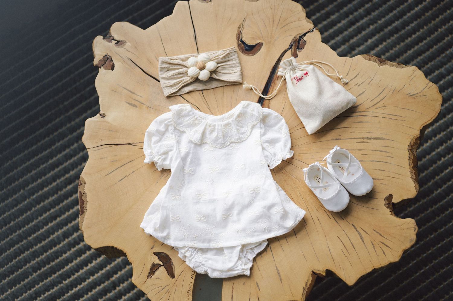 White baby romper with matching bow headband and booties displayed on wooden board surface.