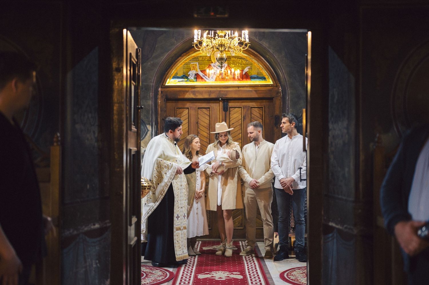 A priest performs a religious ceremony in a traditional Orthodox church doorway under an ornate arched entrance.