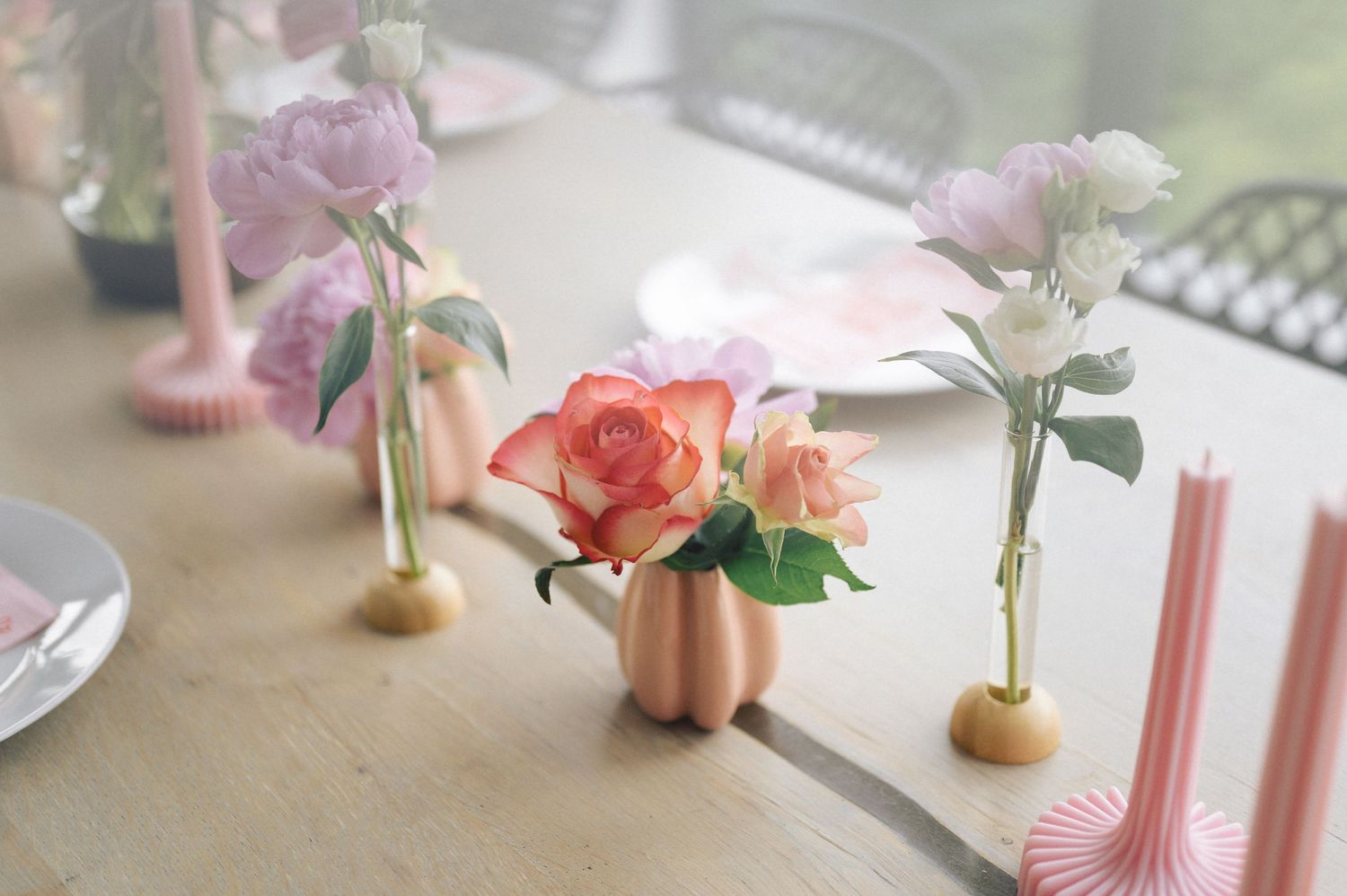 Delicate pink and coral roses arranged in small vases on a light table with a soft, dreamy film photography aesthetic.