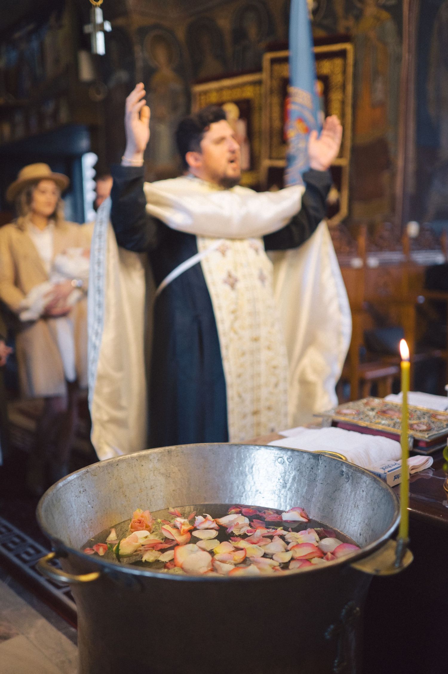 Orthodox clergy member conducts religious ceremony with raised hands while large pot with food sits in foreground.
