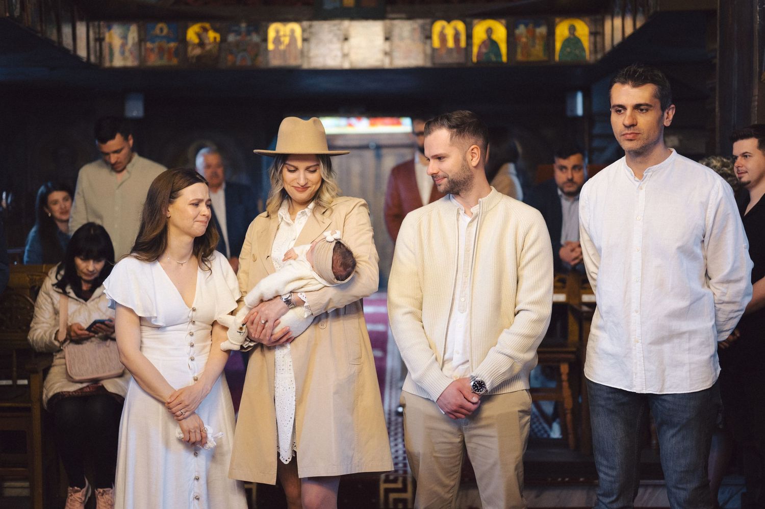 People gather for an indoor ceremony or event wearing light colored attire in a dimly lit venue.