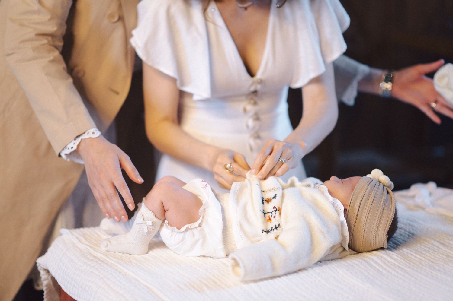 Baby in white dress outfit being dressed on a white changing table while people attend to their needs.