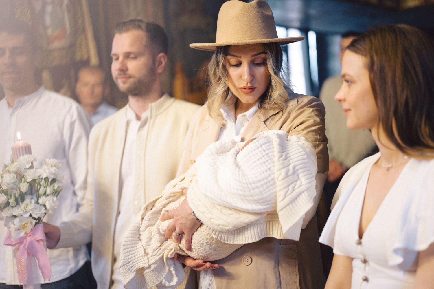 A baptism ceremony gathering where people dressed in white attend a special moment with a baby wrapped in white.