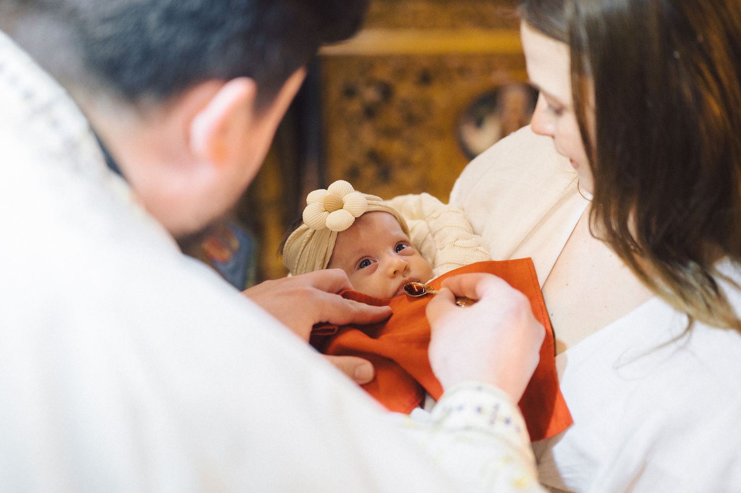 A baby receives holy communion or blessing during a religious ceremony while wearing orange clothing.