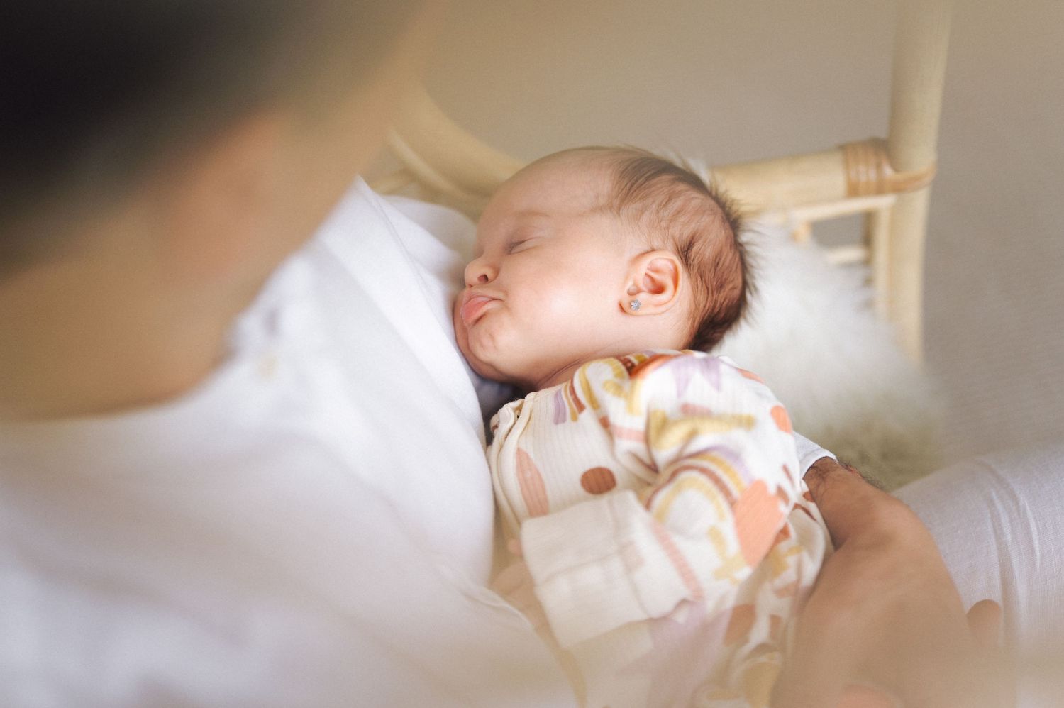 A peaceful sleeping baby in white and peach clothing rests on soft white bedding.