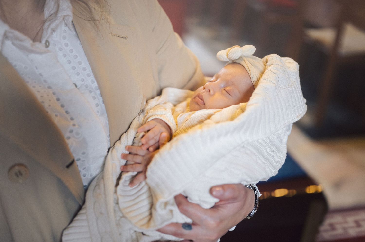 A newborn baby wrapped in white blankets sleeps peacefully while being cradled in arms.