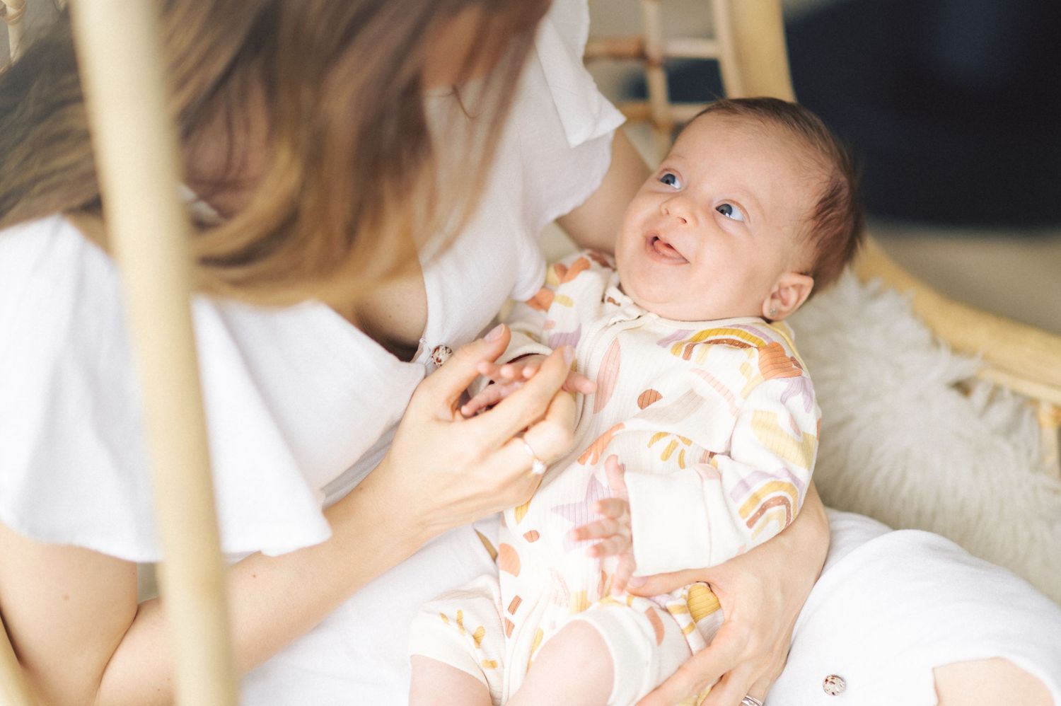 A smiling baby in floral pajamas lying on a couch while being tended to by someone in white.