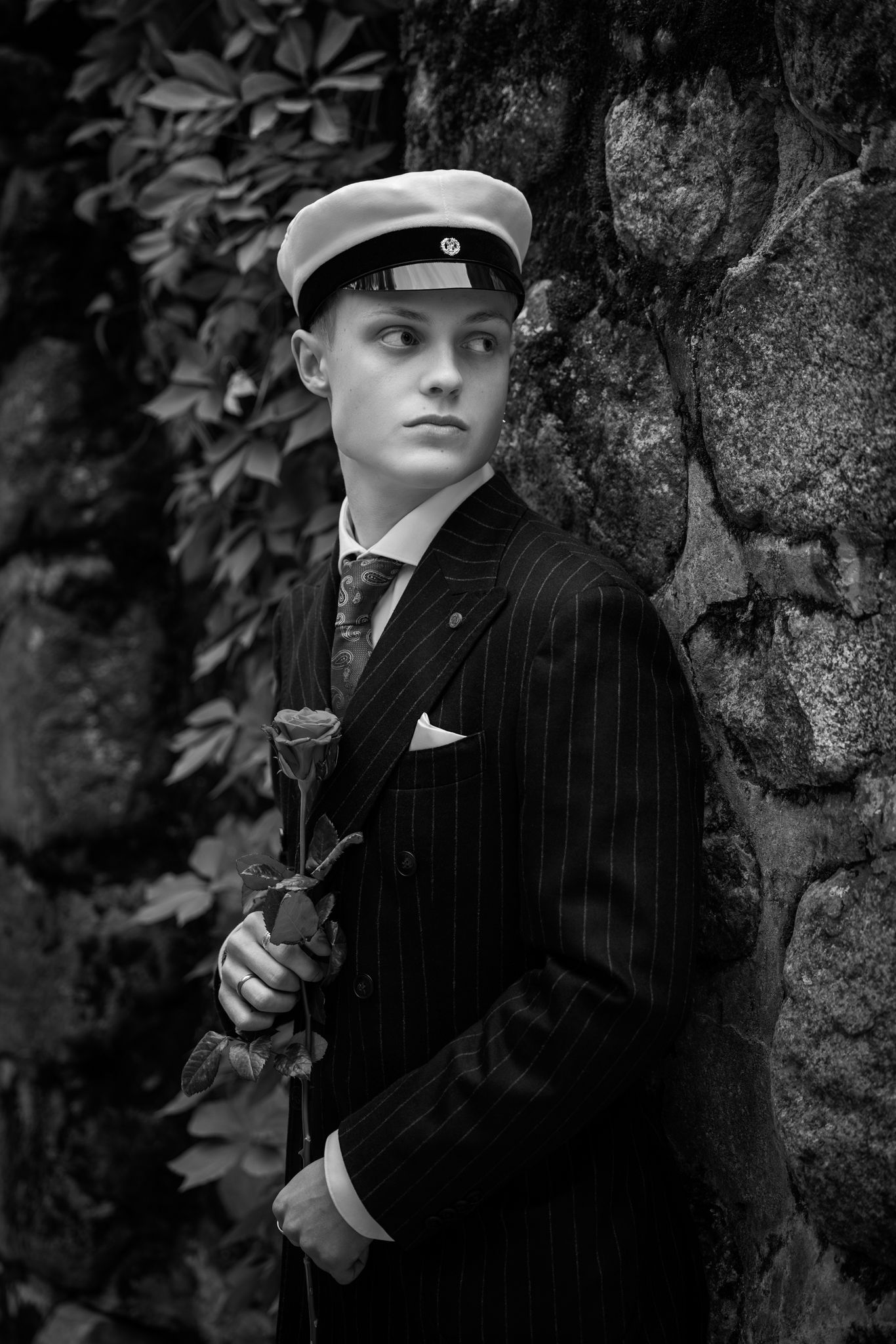 A black and white vintage photo series showing a person in a pinstripe suit and hat posing dramatically against a stone wall.