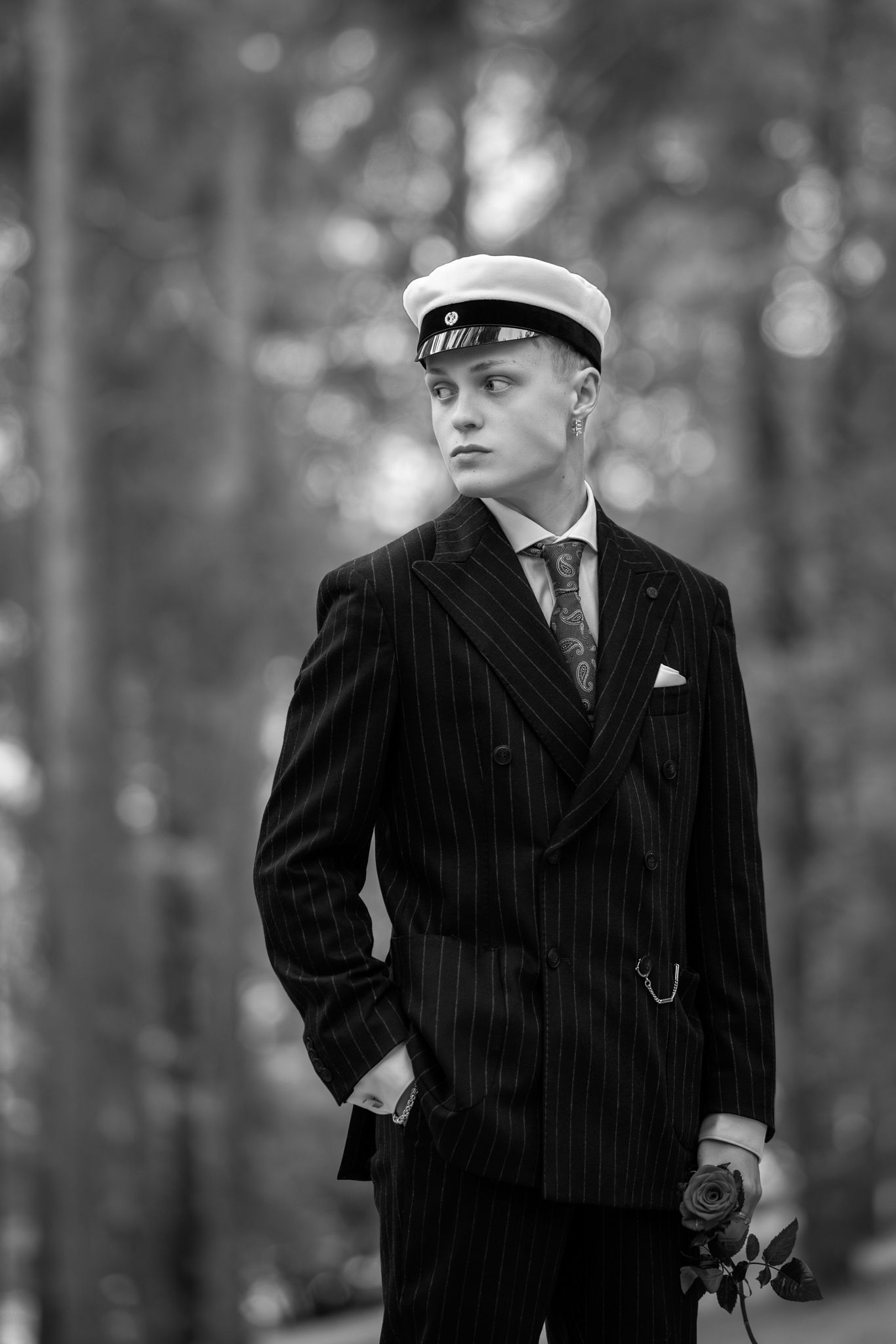 A black and white photograph shows a person in a pinstripe suit and cap standing in a wooded setting.