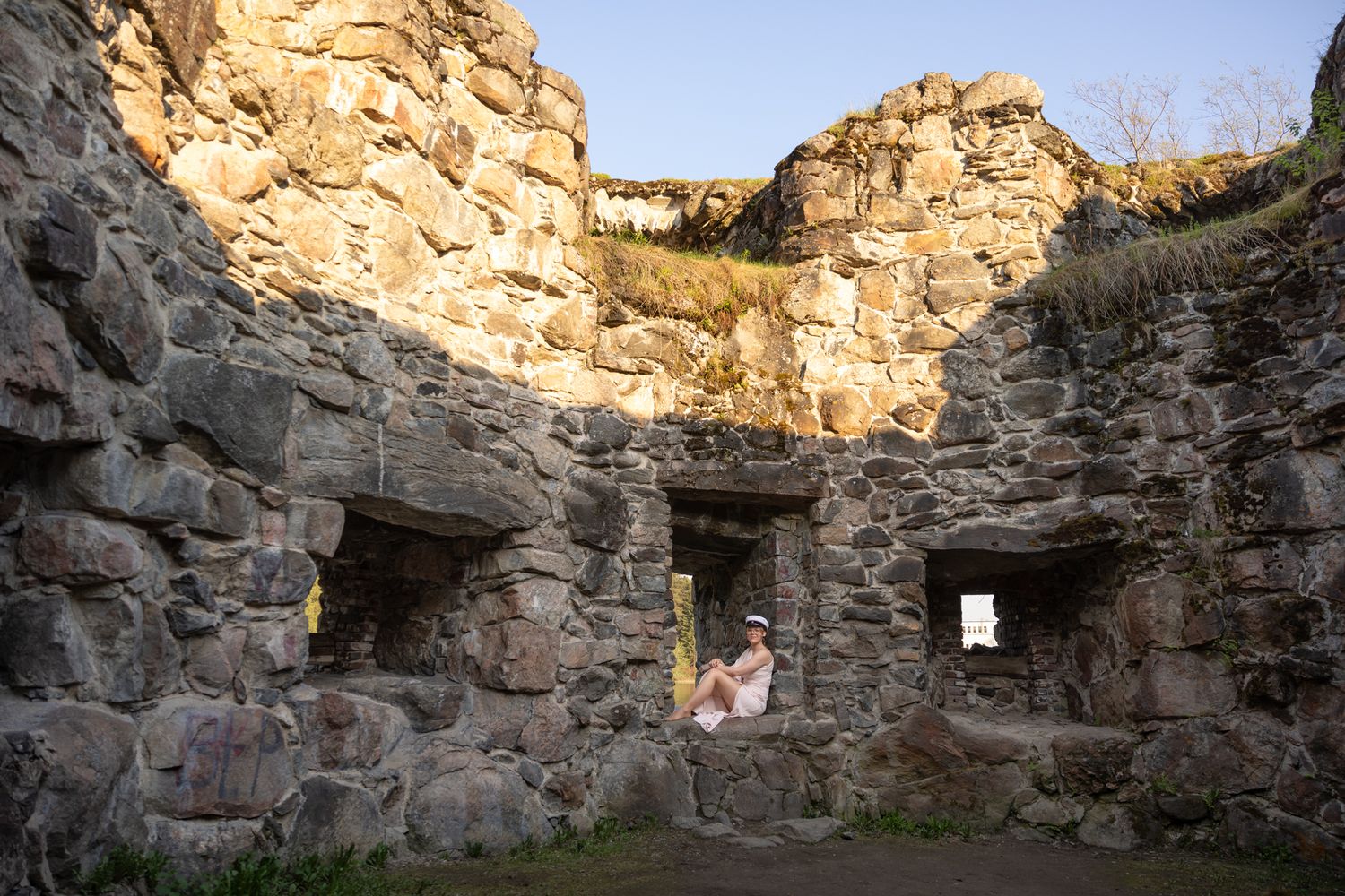 Person sitting inside ancient stone ruins with arched alcoves and weathered rock walls at golden hour.