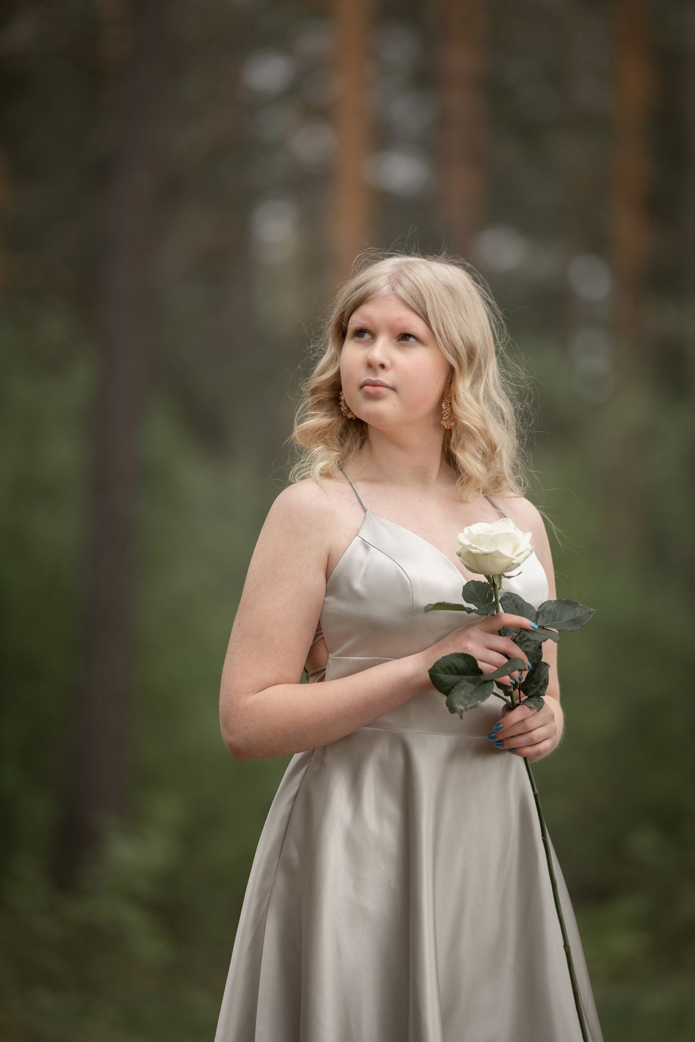 Kullanväriseen mekkoon pukeutunut tyttö käsissään valkoinen ruusu.