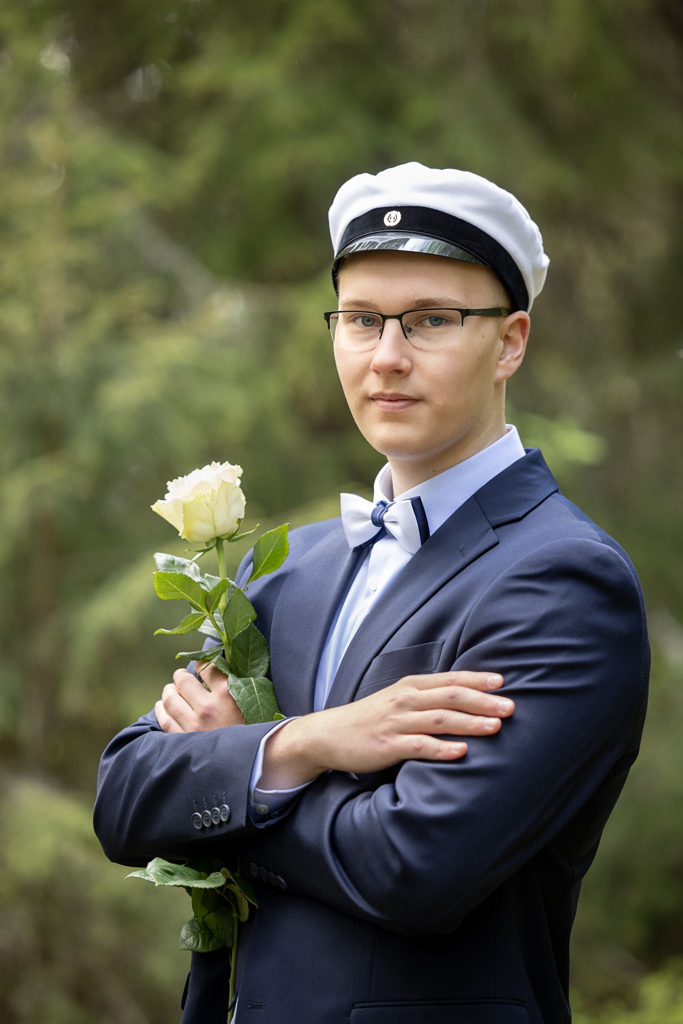 Tummansiniseen pukuun pukeutunut ylioppilas kädessään valkoinen ruusu.