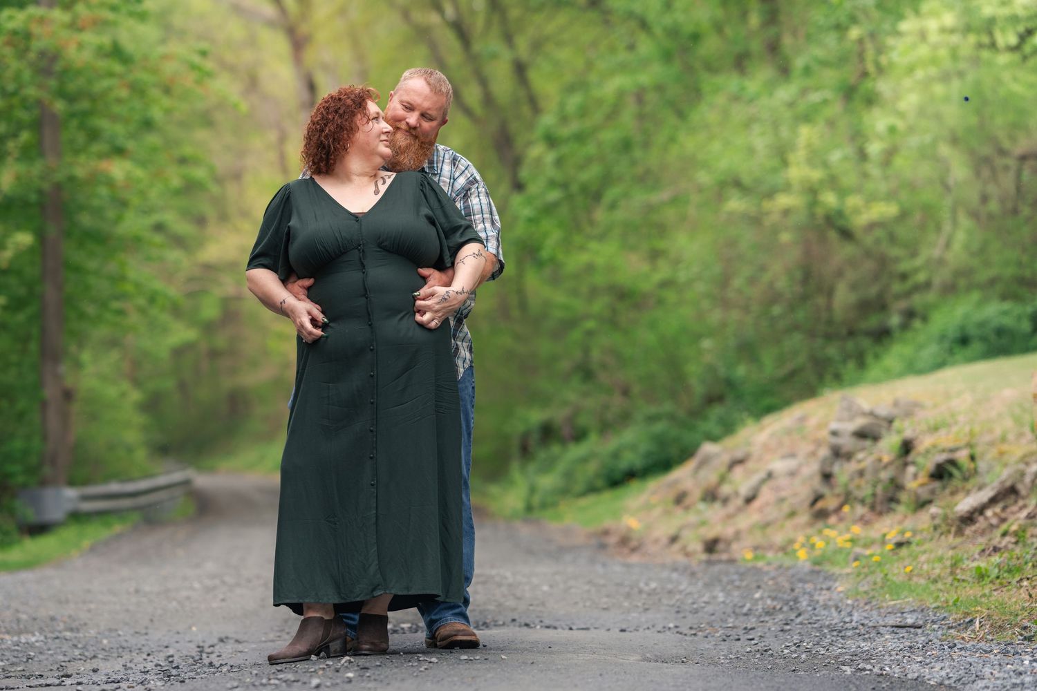 A couple in dark formal attire poses together on a tree-lined path during a romantic outdoor photo session.