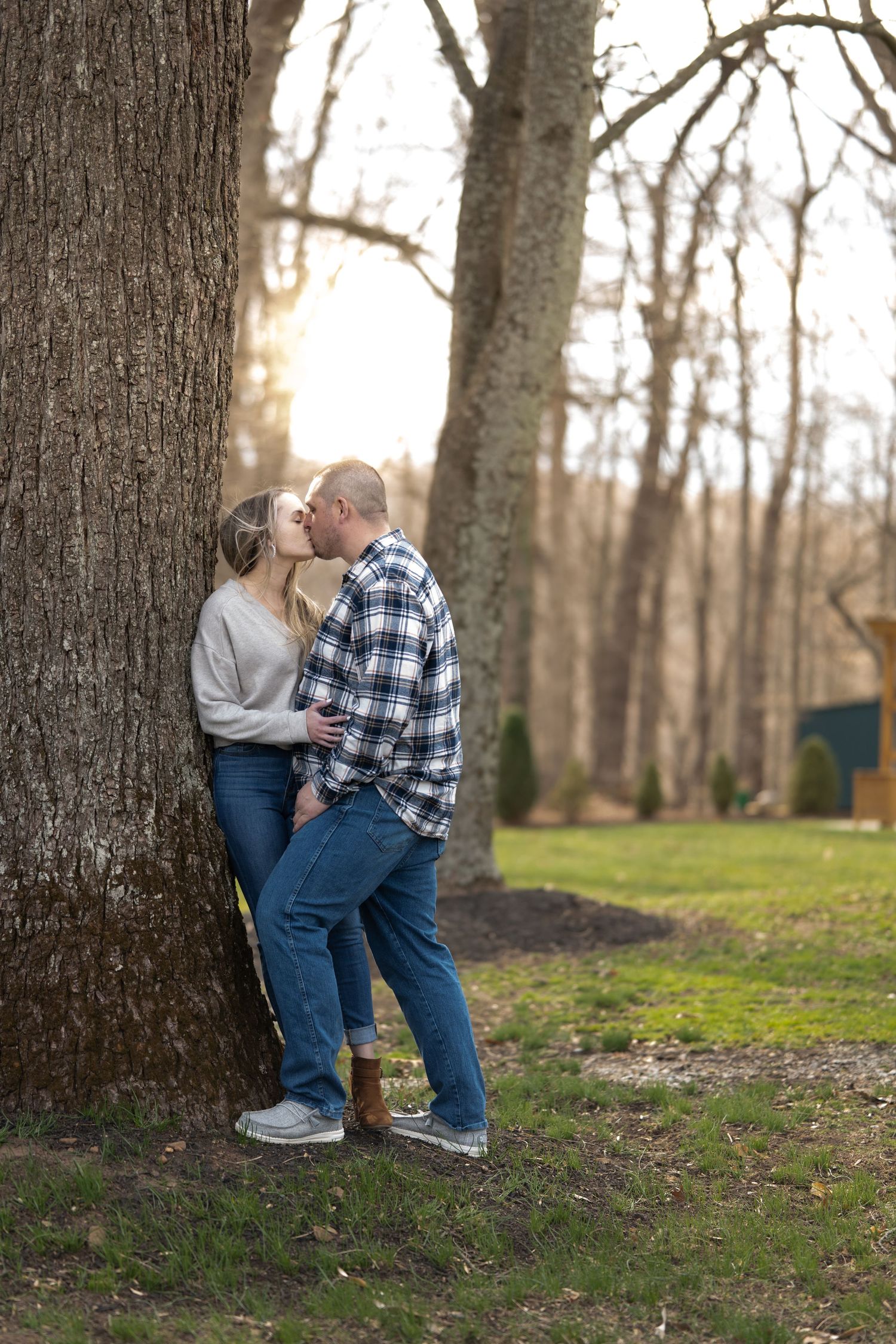 Couple sharing an intimate moment against a large tree trunk in an autumn forest.