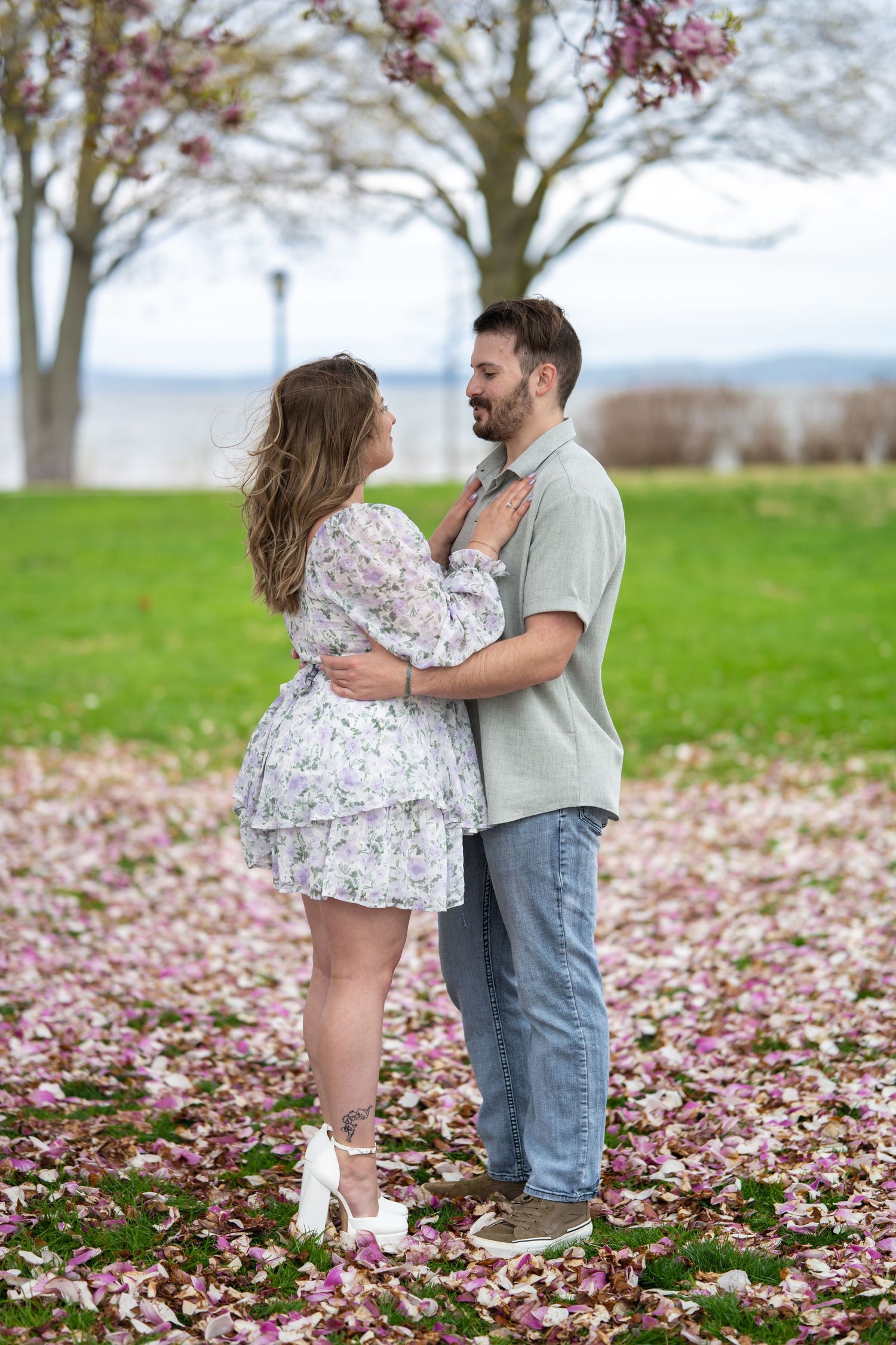 A couple shares a romantic moment together in a field covered with fallen pink cherry blossoms.