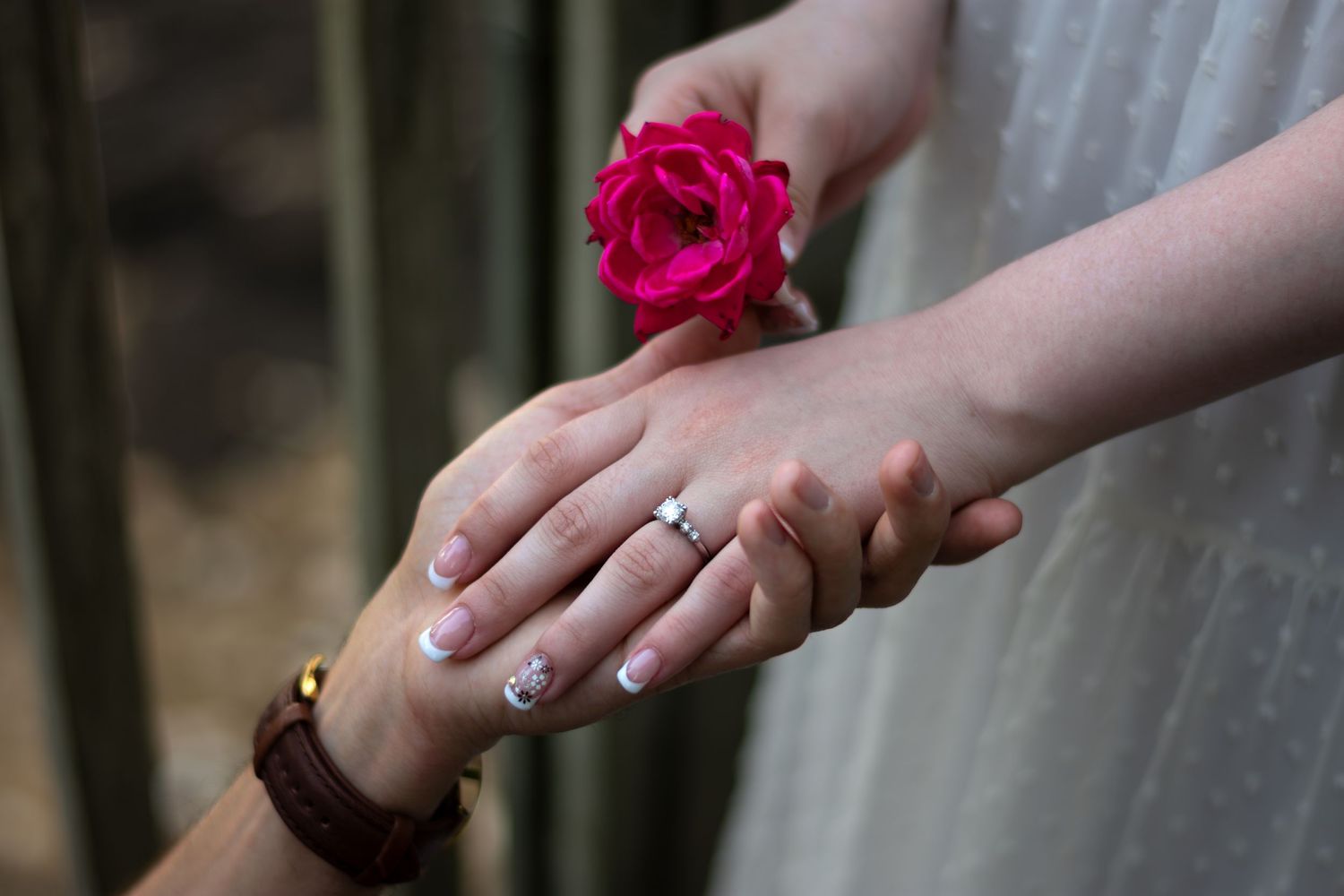 A hand holding a vibrant pink rose against a dark background with soft natural lighting.